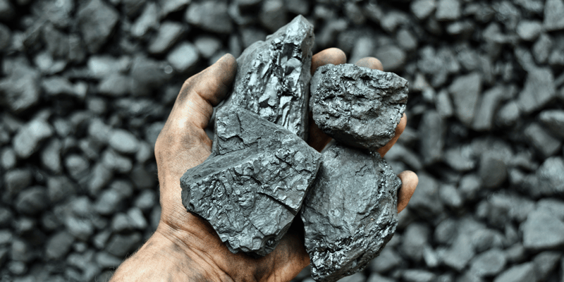 Lumps of coal held in a man's palm.